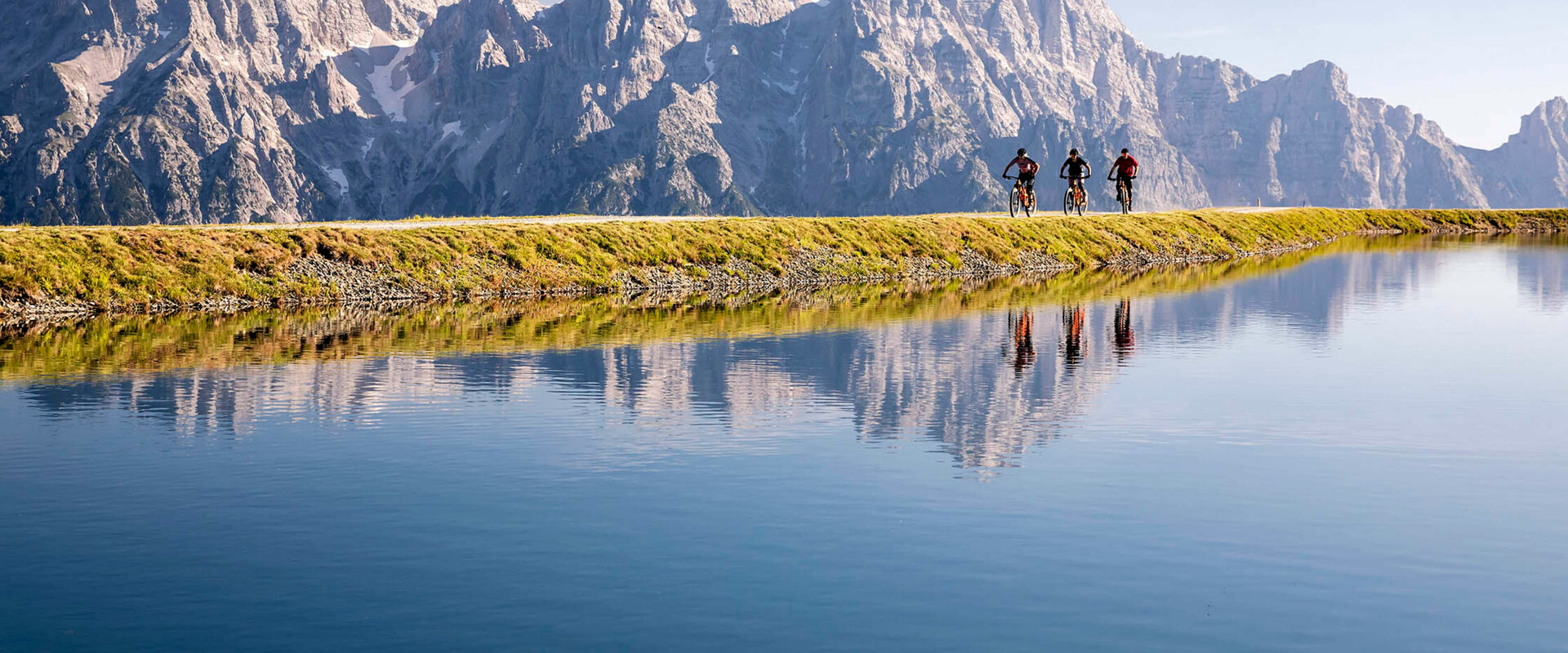 Radfahrer vor Bergkulisse spiegeln sich in See in Leogang
