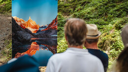 Besucher:innen betrachten eine farbenreiche Bergfotografie entlang des Kunstwanderwegs. | © Michael Geißler