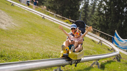 Kind jubelt mit ausgebreiteten Armen bei der Fahrt mit der Klangrodelbahn in Leogang – actionreiches Sommererlebnis für Familien | © Michael Geißler