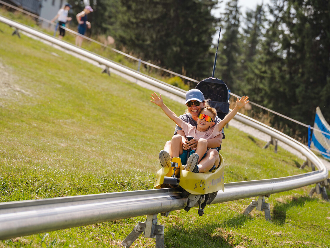 Kind jubelt mit ausgebreiteten Armen bei der Fahrt mit der Klangrodelbahn in Leogang – actionreiches Sommererlebnis für Familien | © Michael Geißler