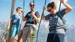 Familie mit Rucksäcken schaukelt am Berg der Sinne in Leogang – aktives Familienerlebnis mit Alpenpanorama in Saalfelden Leogang | © Michael Geißler