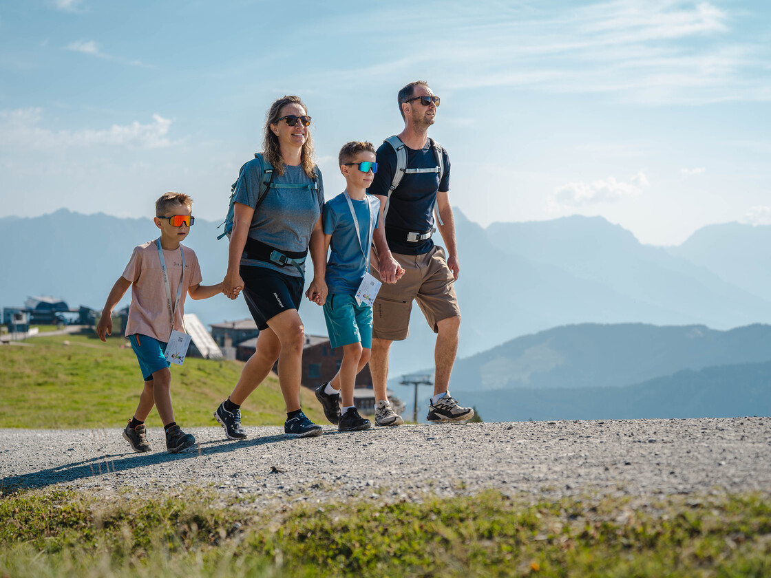 Eltern und zwei Kinder wandern gemeinsam mit Rucksäcken vor beeindruckender Bergkulisse | © Michael Geißler