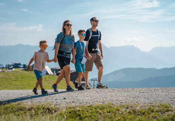 Eltern und zwei Kinder wandern gemeinsam mit Rucksäcken vor beeindruckender Bergkulisse | © Michael Geißler
