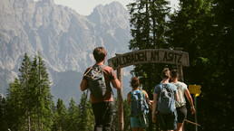ine Gruppe Wander:innen mit Rucksäcken betritt den Waldbaden-Rundweg am Asitz unter einem hölzernen Eingangsschild, umgeben von Wald und Bergpanorama. | © Julia Sapper