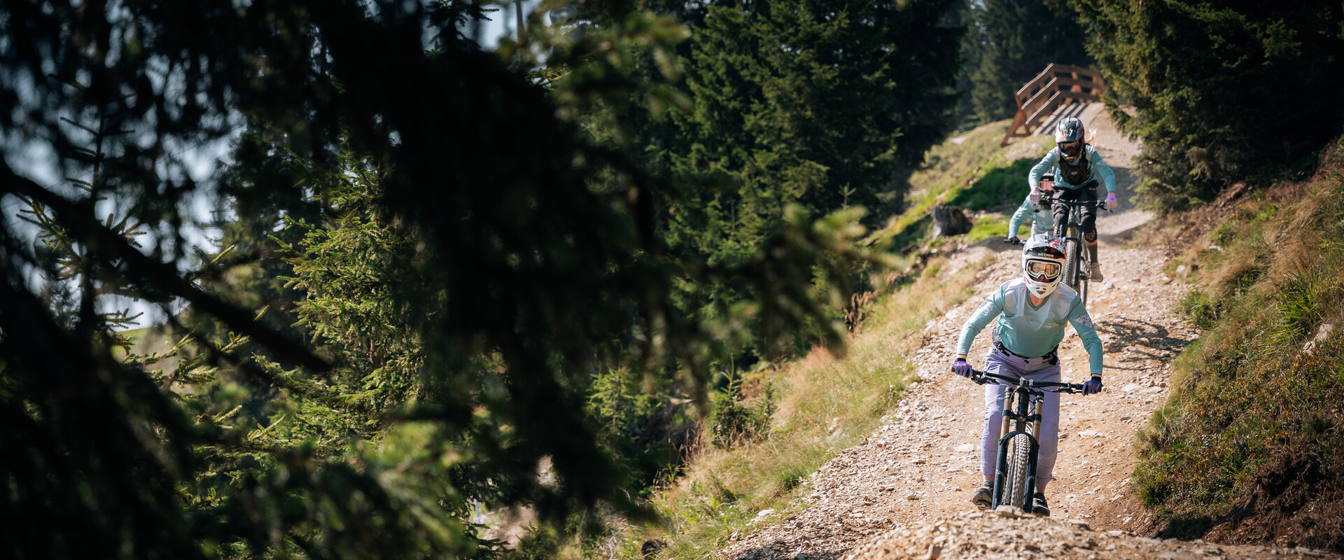 Gruppe von Mountainbiker:innen fährt einen steinigen Trail im Bikepark hinab, eingerahmt von dichten Bäumen und alpiner Landschaft. | © Yvonne Hörl