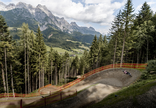 Anlieger mit Aussicht | © Yvonne Hörl Mountainbiker in einem großen Anlieger der T-Line, die sich durch den Wald schlängelt. Im Hintergrund das beeindruckende Panorama der Leoganger Steinberge. | © Yvonne Hörl
