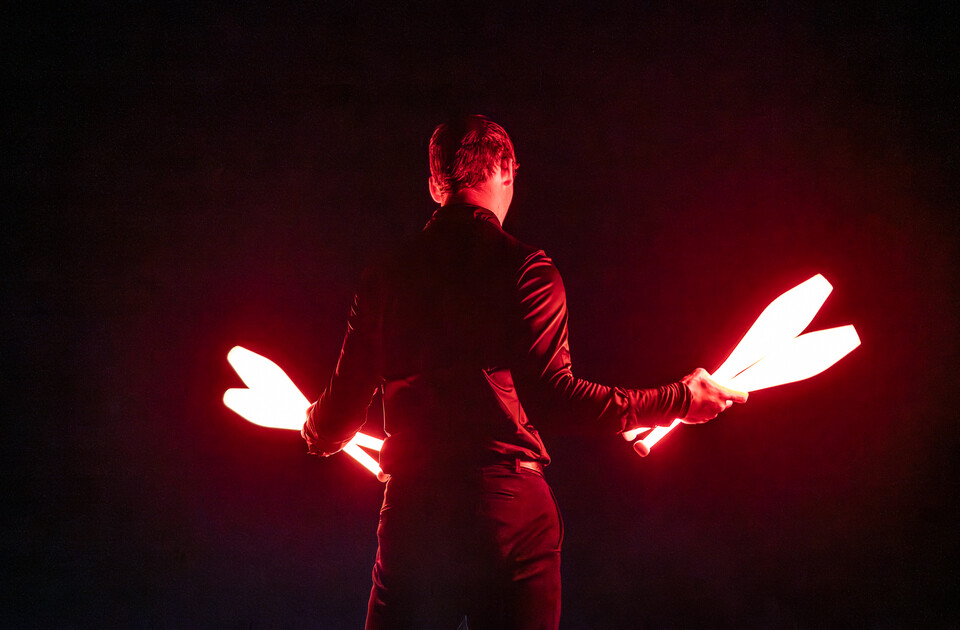 Ein Mann steht vor schwarzem Hintergrund mit mehreren LED-Keulen in der Hand, die zum Jonglieren dienen.  | © cb photography