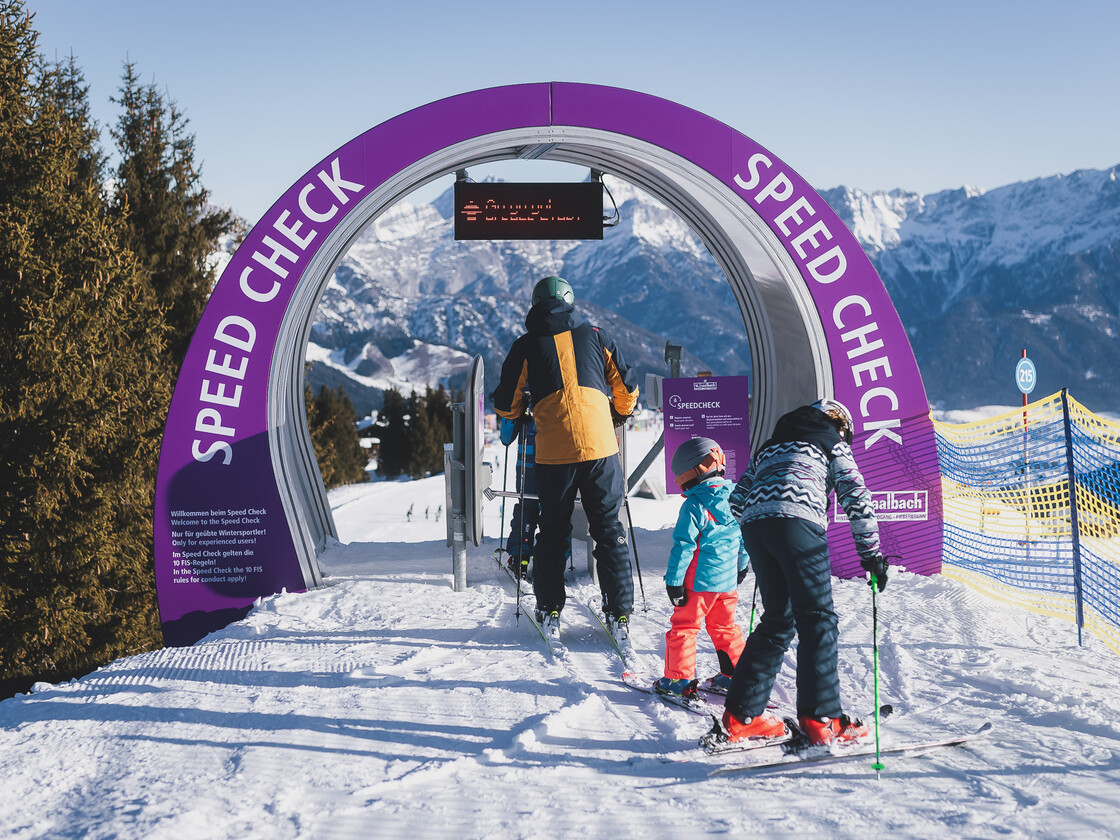 Zwei Skifahrer stehen am Rand einer Funslope und schauen auf die Strecke mit ihren Hindernissen und Spaß-Elementen. Im Hintergrund eine verschneite Landschaft mit Berggondeln. | © Stefanie Oberhauser