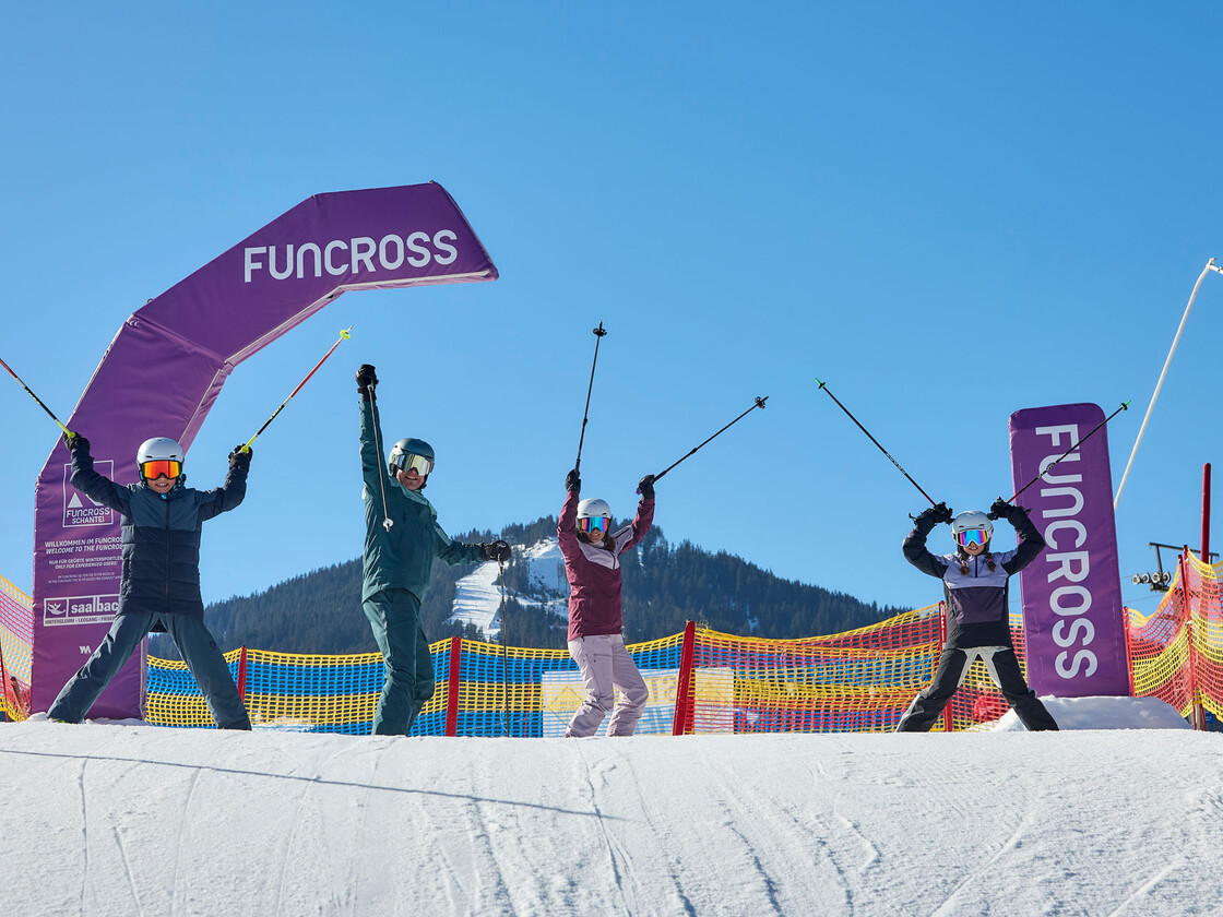 Vier Skifahrer jubeln unter dem Funcross-Bogen am Schanteilift in Leogang und genießen das Familienangebot im Skicircus Saalbach Hinterglemm Leogang Fieberbrunn. | © Daniel Roos