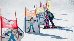 Üben mit Motivation: Ein Kind meistert mit Begleitung die Hindernisstrecke im Kinderland Leogang – perfekter Einstieg ins Skifahren. | © Michael Geißler