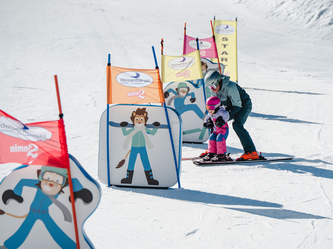 Üben mit Motivation: Ein Kind meistert mit Begleitung die Hindernisstrecke im Kinderland Leogang – perfekter Einstieg ins Skifahren. | © Michael Geißler