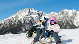 Mama und Kinder rodeln gemeinsam auf der Tagesrodelbahn am Asitz in Leogang vor beeindruckender Alpenkulisse | © cb photography / Christoph Bayer
