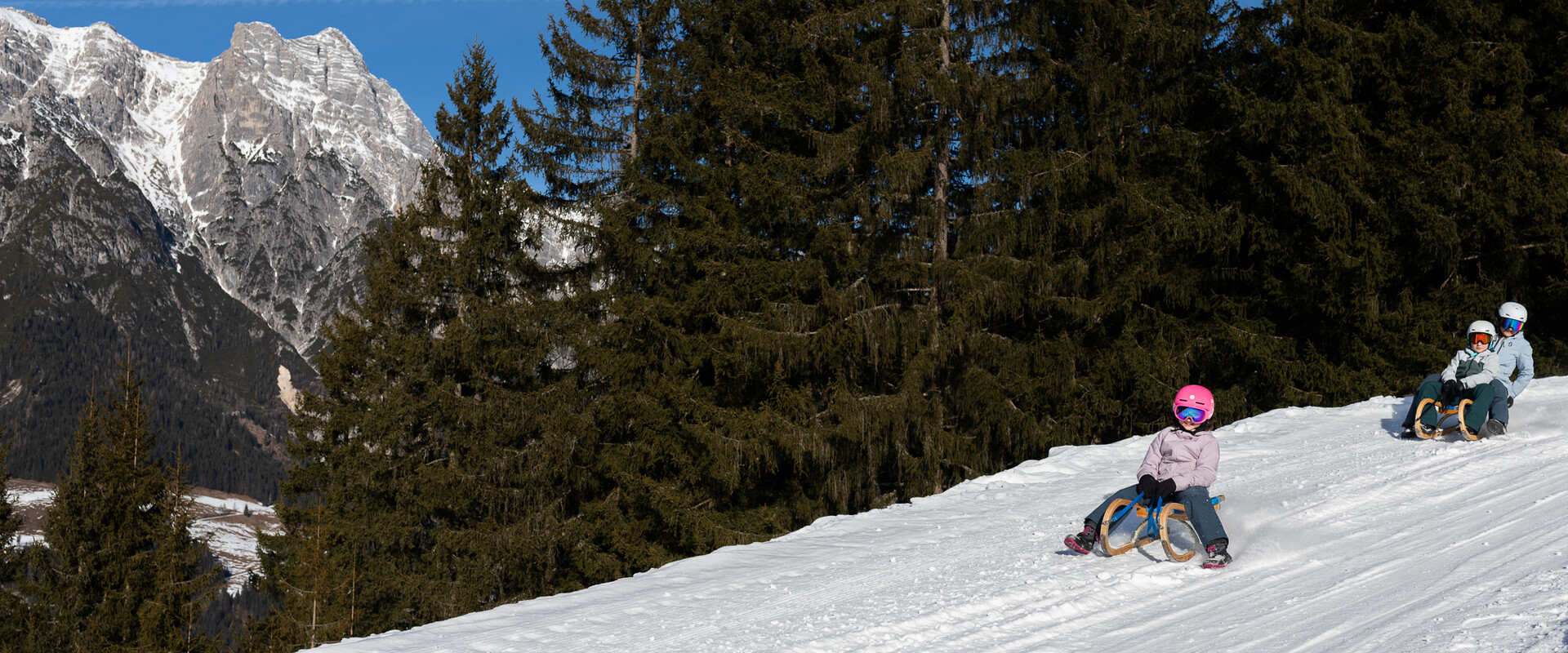 Personen fahren mit Rodel die verschneite Rodelstrecke am Asitz in Leogang hinunter – Wintererlebnis für die ganze Familie | © cb photography / Christoph Bayer